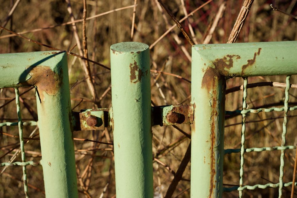 Close up of a painted steel fence with rust breaking through at the joints