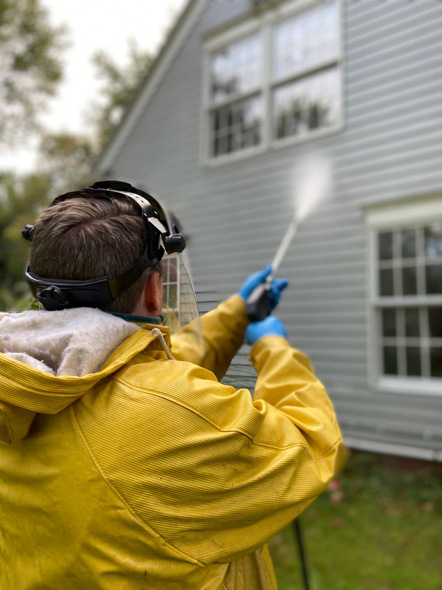 A worker in protective gear pressure washing the exterior wall of a house