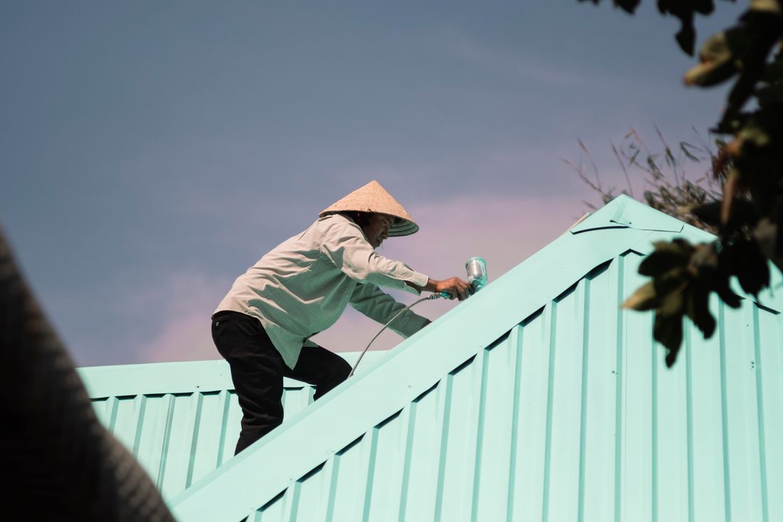 A painter spraying a corrugated metal roof with fresh coating