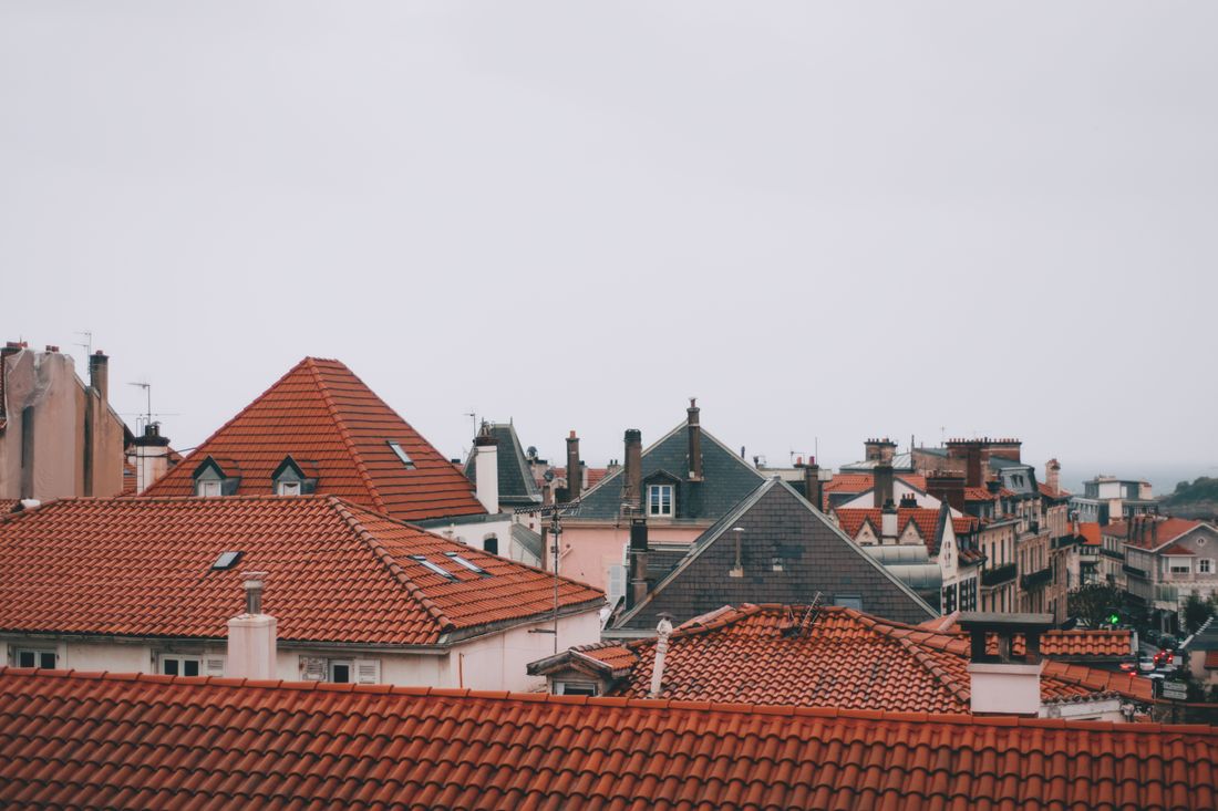 Aged residential roofs under a grey sky, tiles darkened and weathered
