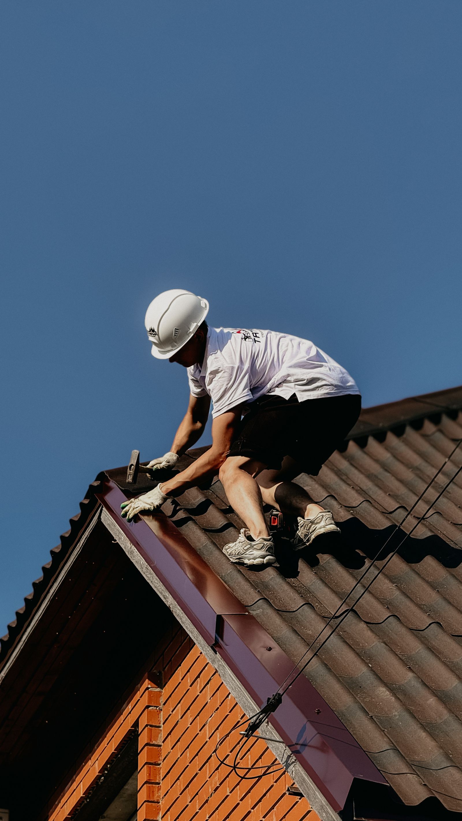 A roofer in a hard hat fixing the barge flashing on a tiled roof