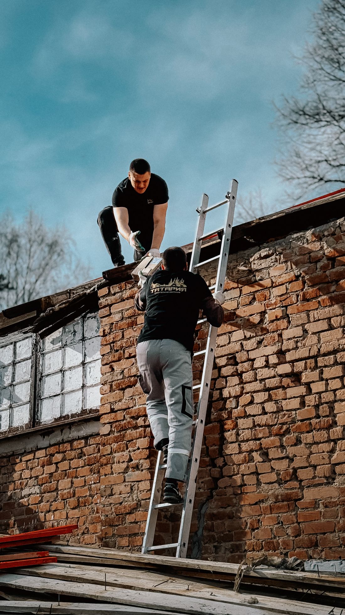 Two roofers climbing a ladder onto a brick building to begin an inspection